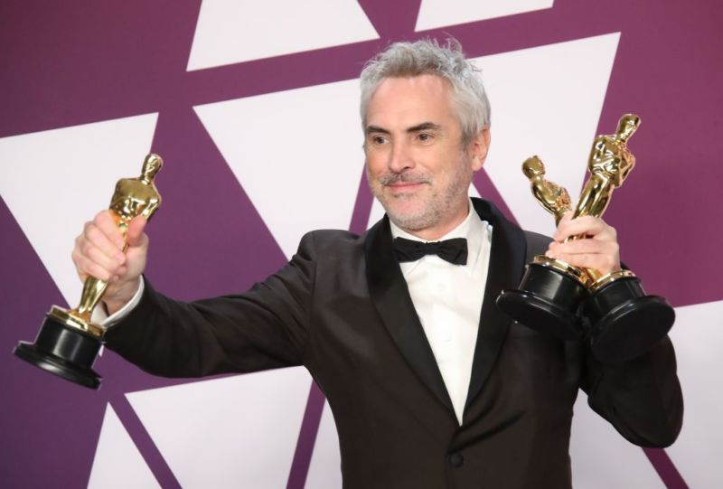 Roma director Alfonso Cuaron holding three Oscars trophies.