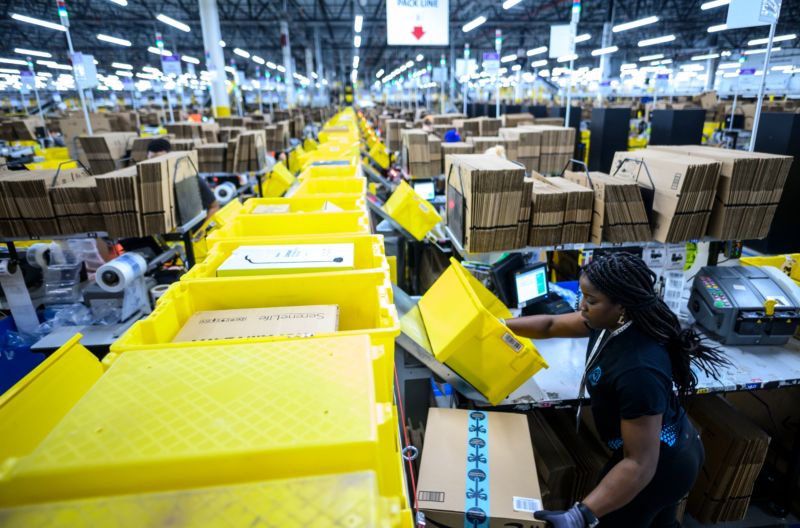 A woman works at a conveyor belt in a gigantic warehouse.