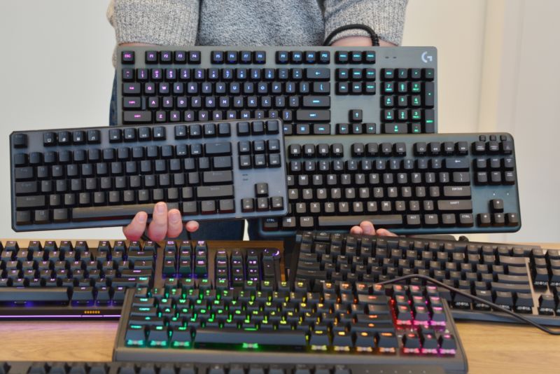 A person whose head is cropped from the photo poses with 6 computer keyboards.