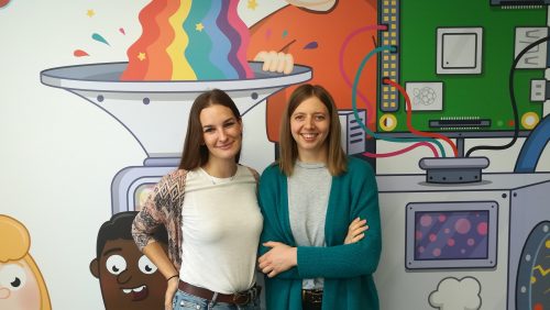 two smiling women standing in front of a colourful wall