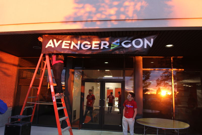Out-of-uniform soldiers attach banner of glass doors of convention center.