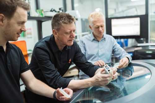 Photo of three people sitting at a table in an office handling and discussing 3D-printed Raspberry Pi case prototypes
