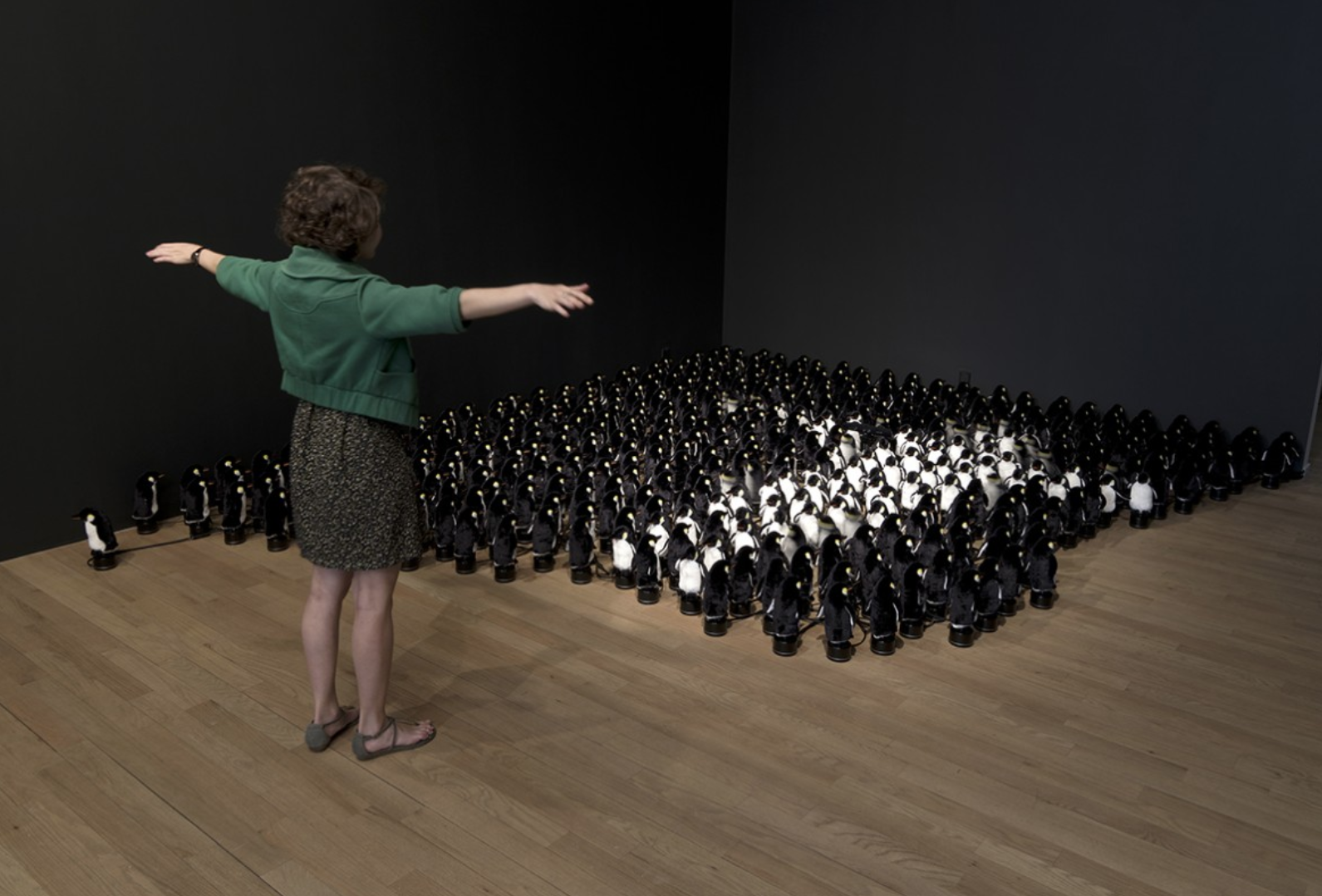A woman standing in front of a mechanical mirror made of toy penguins