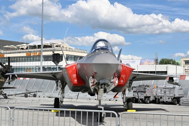 A jet fighter its on a runway behind low metal fencing.