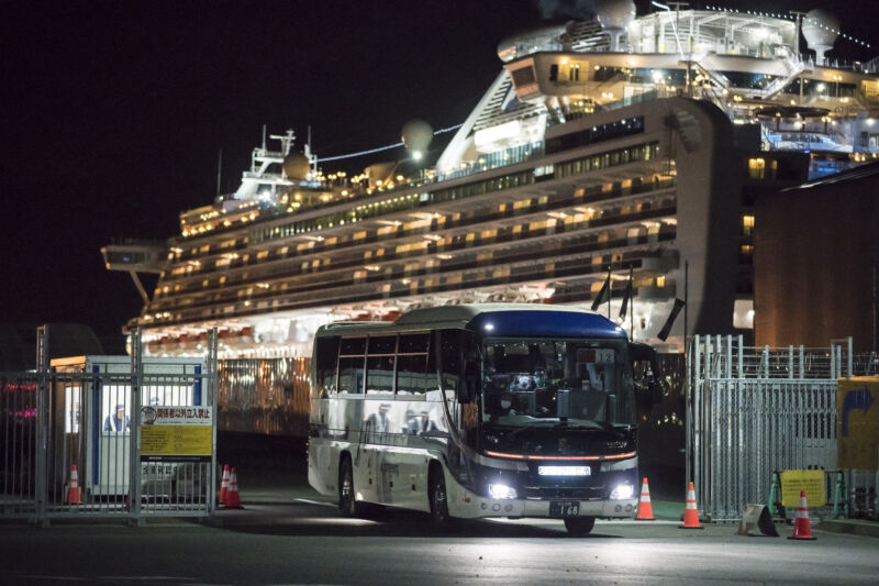 A charter bus drives away from a cruise ship at night lit up like a Christmas Tree.