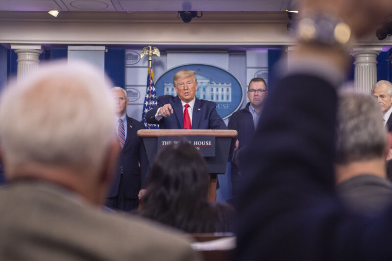 A man in a suit speaks at a podium.