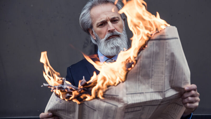 Stock photo of a gloriously bearded man reading a newspaper that's on fire.