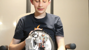 The inventor of the clock holds it with the back facing the camera to show us how it works and is looking down at it.