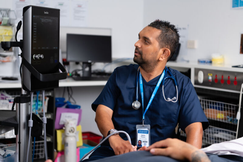 A seated doctor regards a medical device.