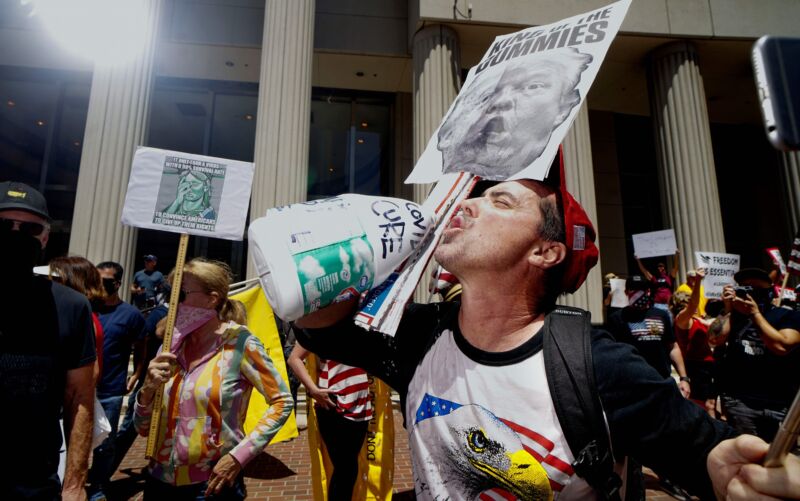 A demonstrator holding an anti-Trump sign, pretends to drink from a bottle of bleach during a rally to re-open California and against Stay-At-Home directives on May 1, 2020 in San Diego, California.
