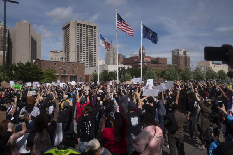 Crowds gather in the shadow of skyscrapers.