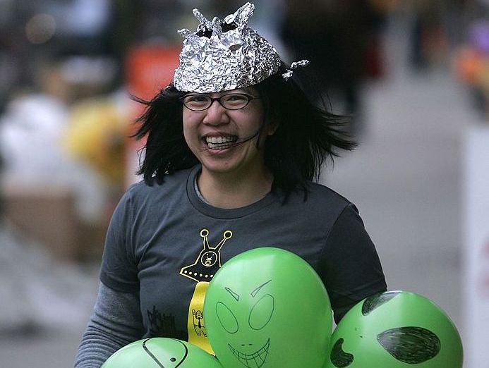 A laughing woman wears a hat made of tin or aluminum foil as she walks down a street.