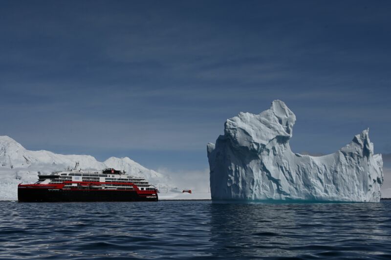 View of an iceberg and the Hurtigruten hybrid expedition cruise ship MS Roald Amundsen on Half Moon island, Antarctica on November 09, 2019.