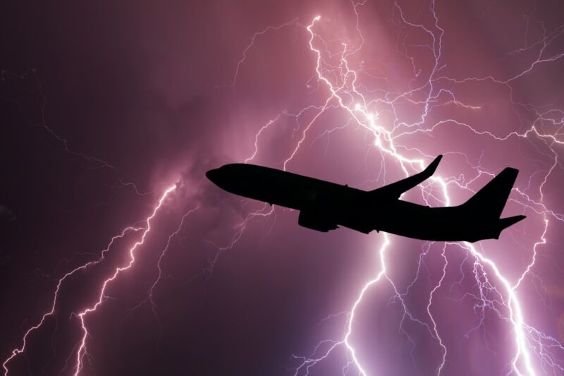 A passenger jet is gloriously silhouetted by a lightning storm.