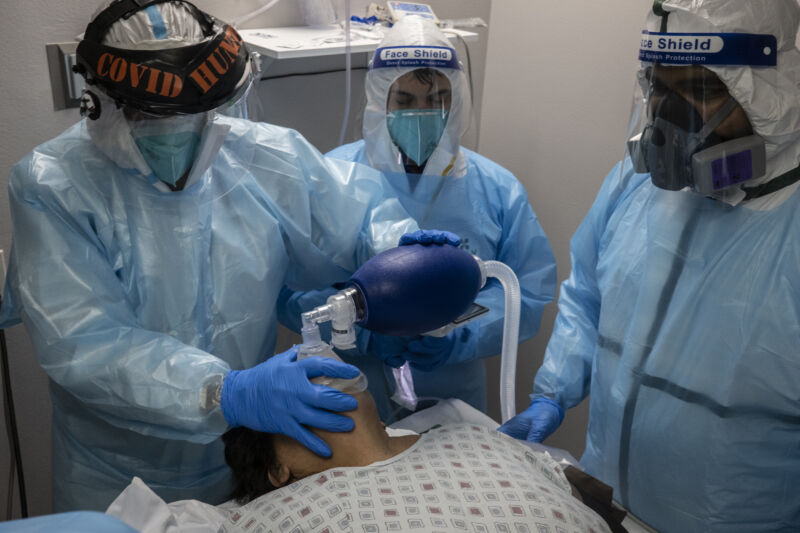 Medical workers in protective gear apply a breathing apparatus to a recline patient.