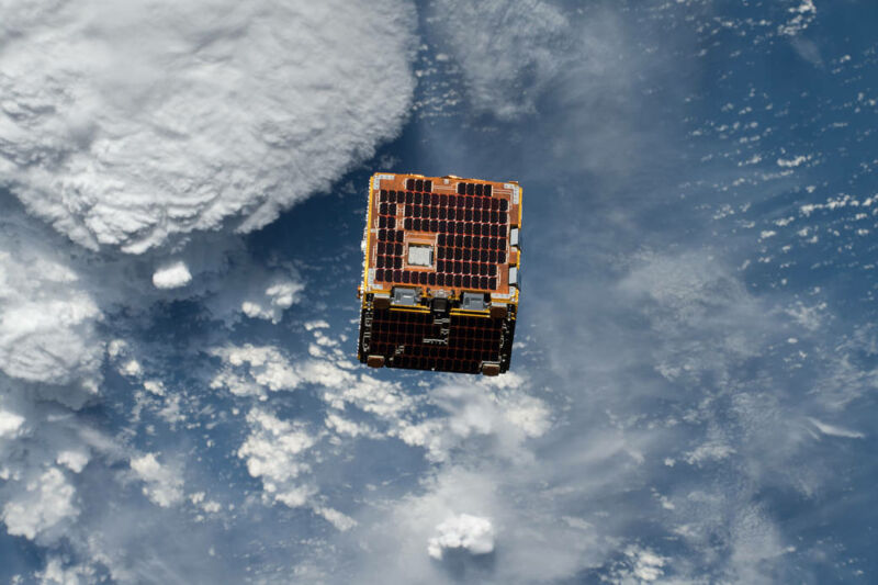 A cube covered in solar panels orbiting above clouds.