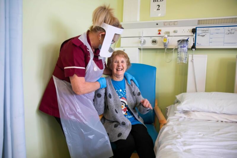 Margaret Keenan, 90, who was the first patient in the United Kingdom to receive the first of two doses of the Pfizer-BioNTech COVID-19 vaccine, reacts as she talks with healthcare assistant Lorraine Hill, while preparing to leave University Hospital Coventry, in Coventry on December 9, 2020, a day after receiving the vaccine.