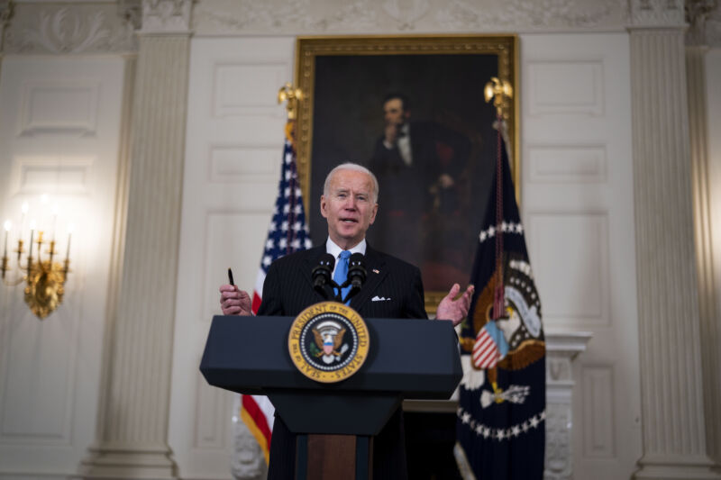 An older man in a suit speaks at a podium in front of a portrait of the Great Emancipator.