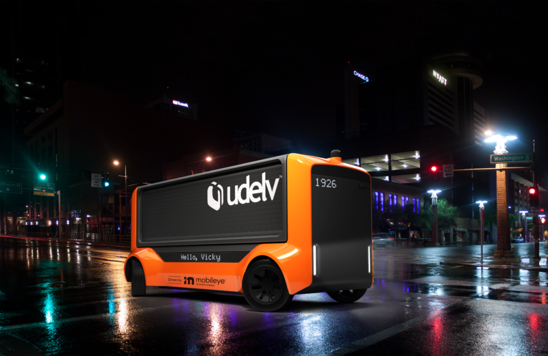 A Udelv-branded van roams wet streets at night.