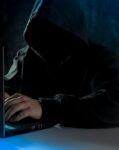 anonymous computer hacker in hoodie using laptop