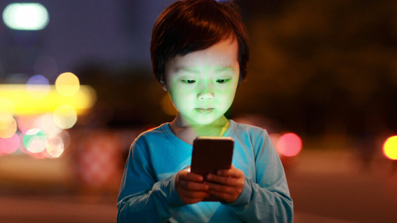 A child on streetside is fascinated by what is on a smartphone.
