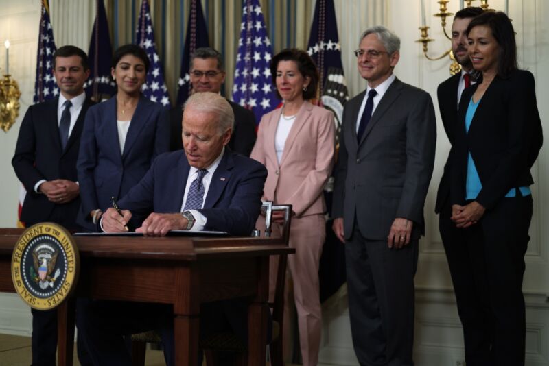 Joe Biden signs an executive order surrounded by various administration officials, including FCC Acting Chairwoman Jessica Rosenworcel.