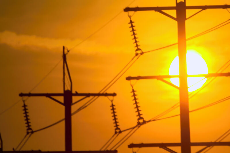 Image of electrical power lines against a backdrop of a warm, orange sky.
