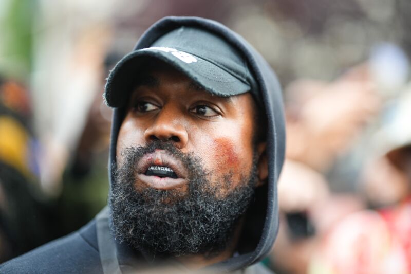 Kanye West wearing a baseballl cap, hooded sweatshirt, and a mouthguard.