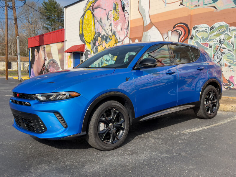 A blue Dodge Hornet parked next to the outside of a bowling alley covered in street art
