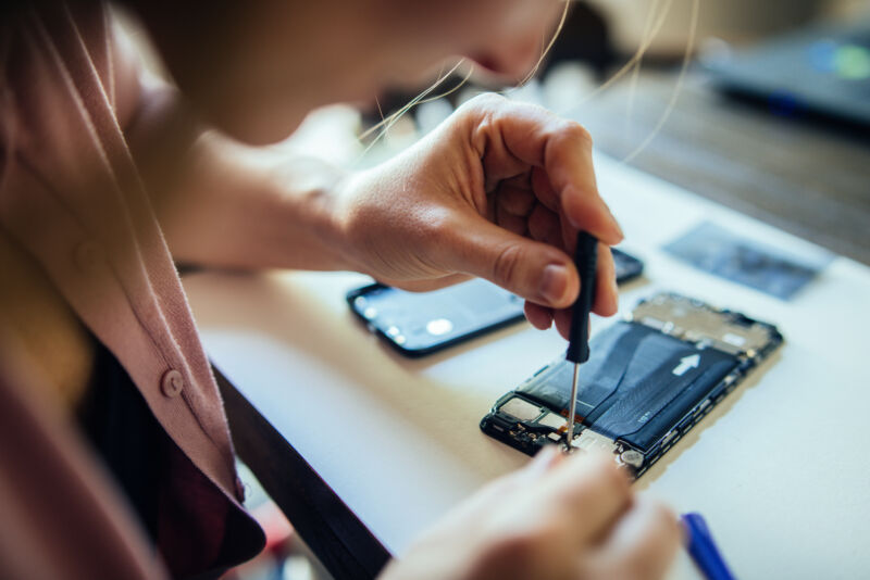 Woman repairing mobile phone at home, changing damaged part.