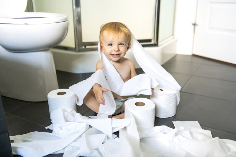 Toddler ripping up toilet paper in bathroom