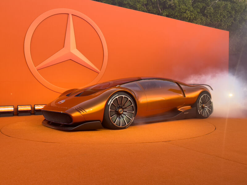 An orange Mercedes concept car next to an orange background. There's some dry ice fog behind it