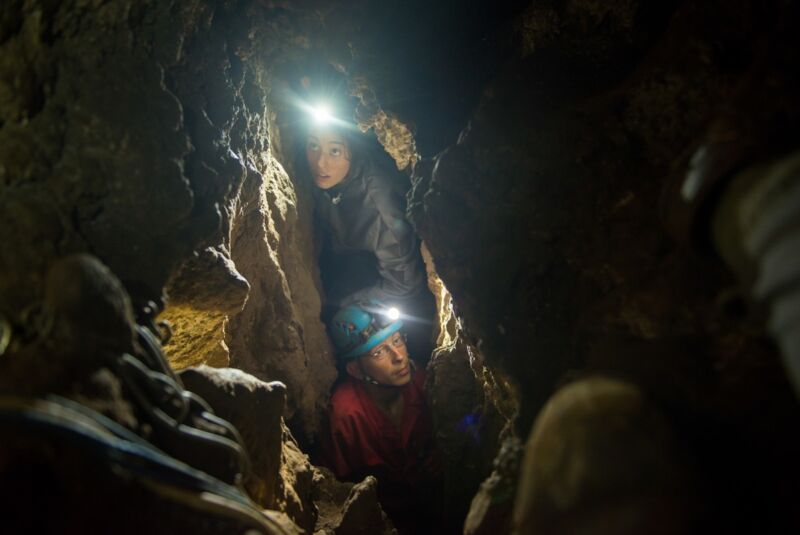 Man and woman navigating narrow chutes in cave