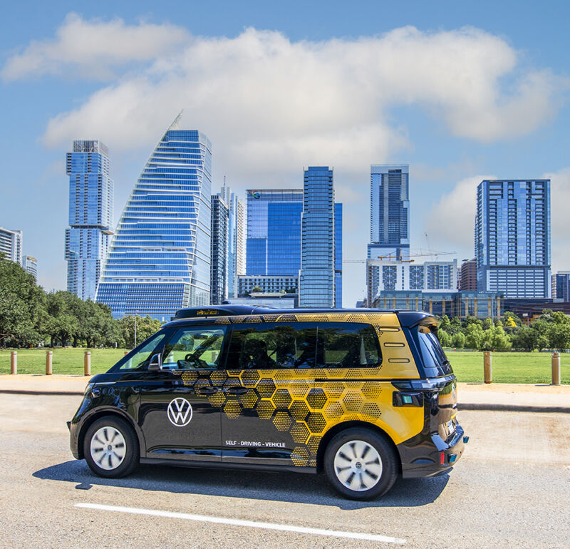 A black and gold VW ID. Buzz with sensors on its roof and Austin's skyline in the background