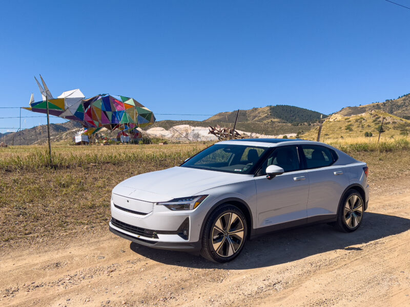 A white polestar 2 parked next to a colorful sculpture of a triceratops