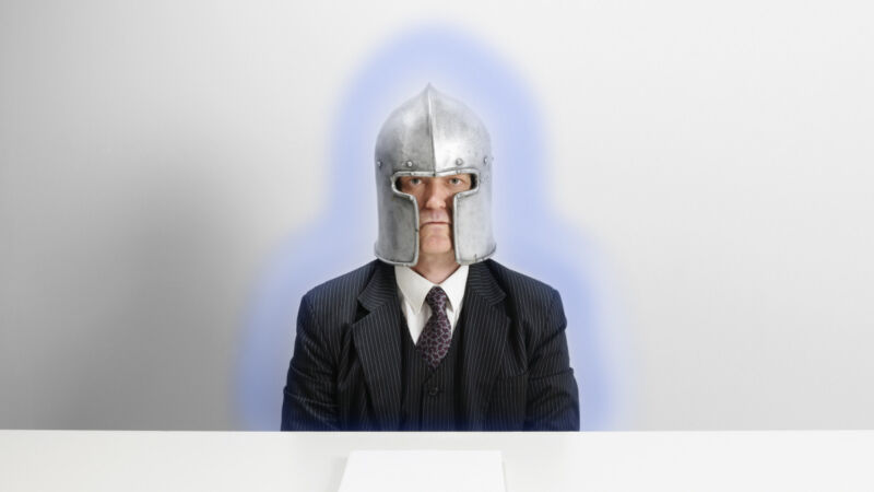 A man in an armor helmet sitting at a desk with a protective glowing field around him.