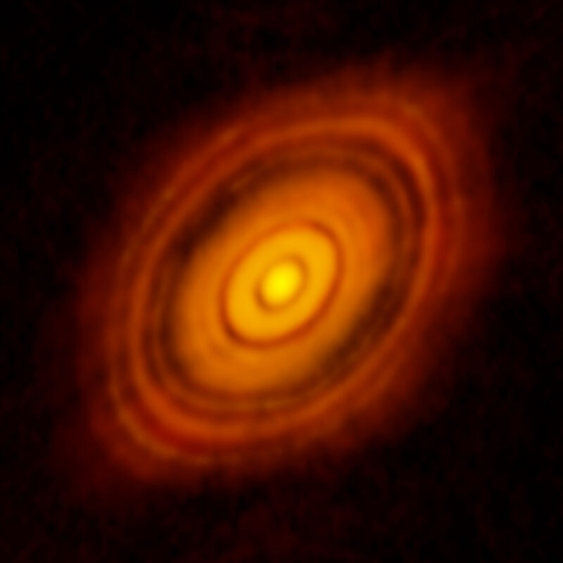 Image of an orange, circular shape, with a bright object at the center and areas of higher and lower brightness.