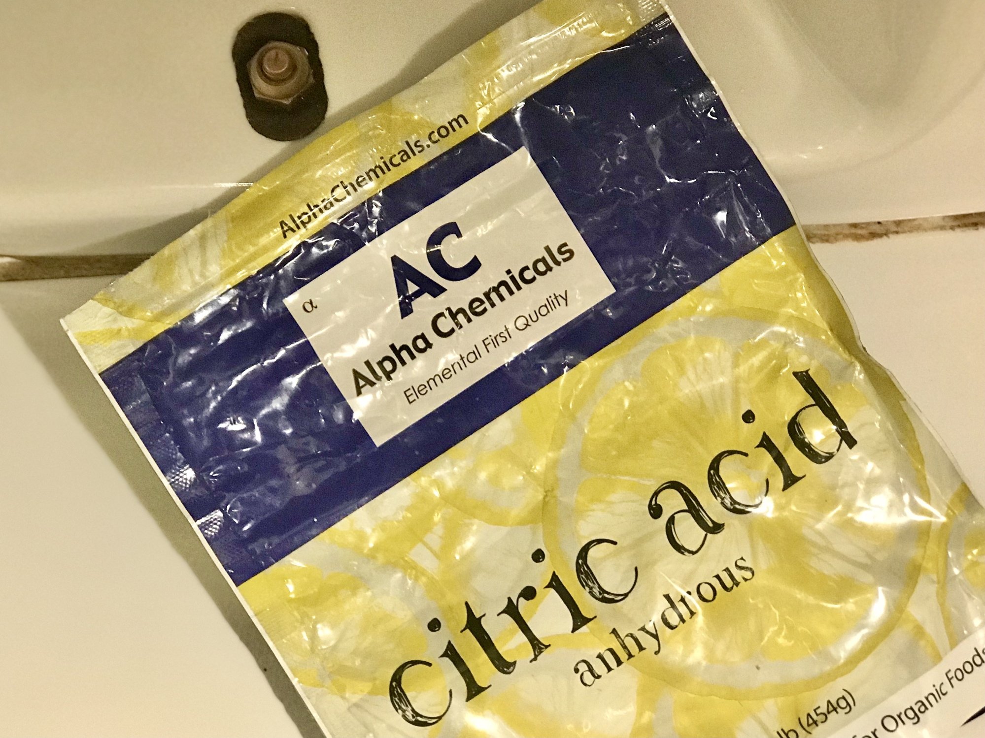bag of citric acid near bottom of toilet on white tile floor