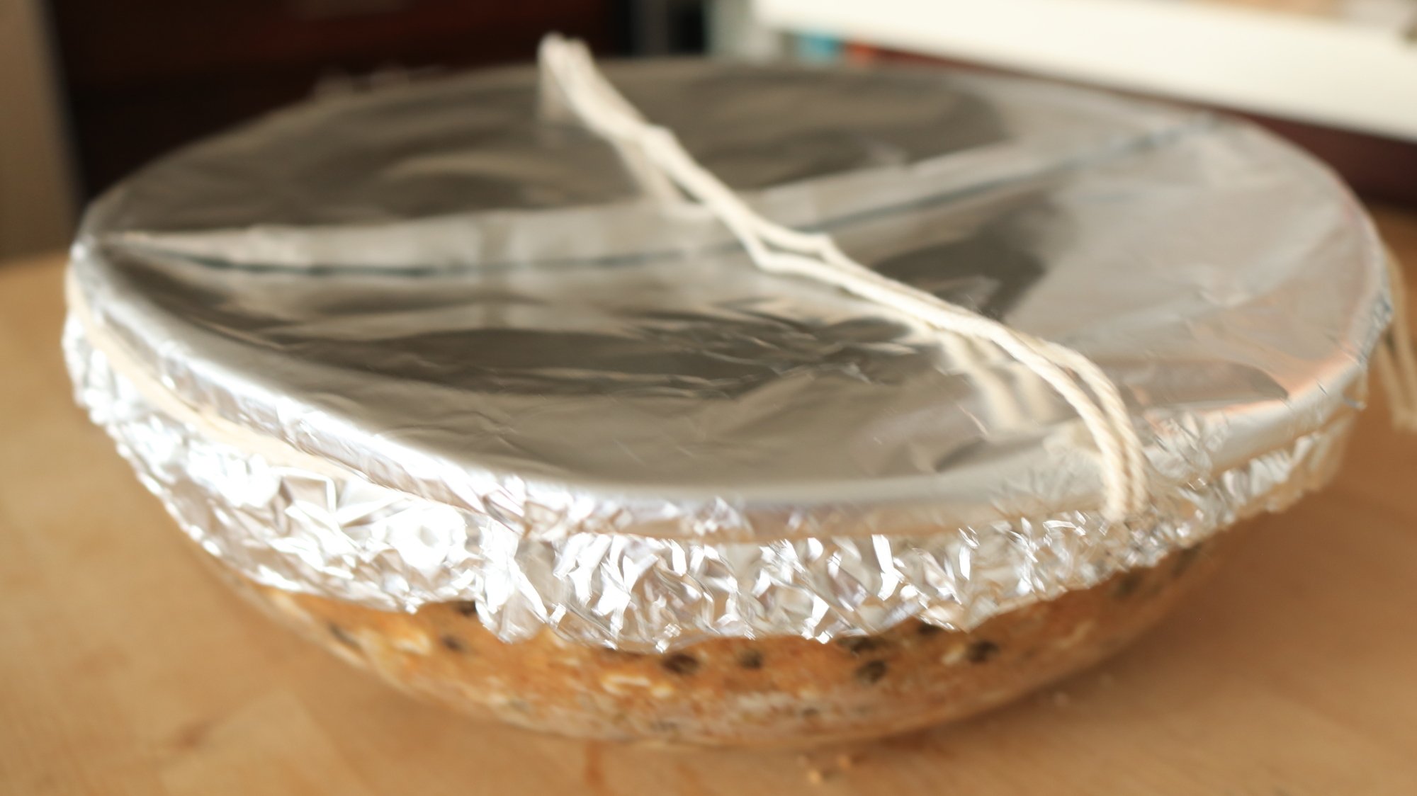 A bowl with foil over the top and string sealing it shut around the edges.