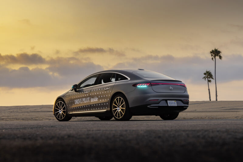 A grey Mercedes EQS seen at sunset at the beach, it has turquoise lights in its tail lamps