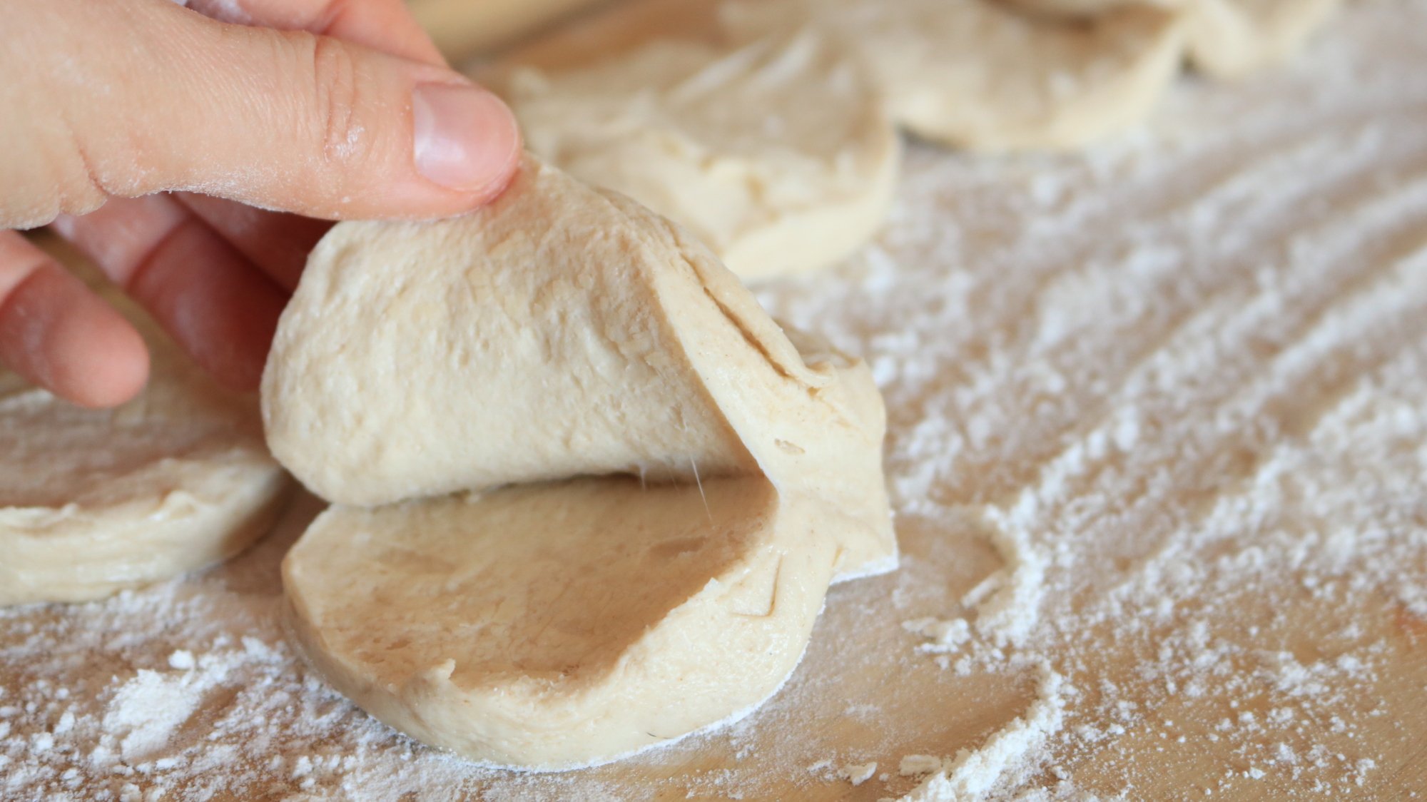 Hand peeling raw biscuit dough in half.