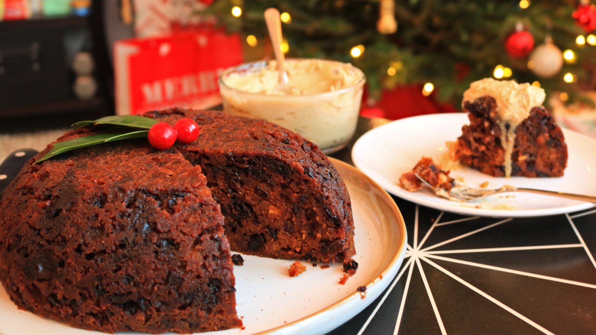A Christmas pudding next to a slice served with brandy butter.