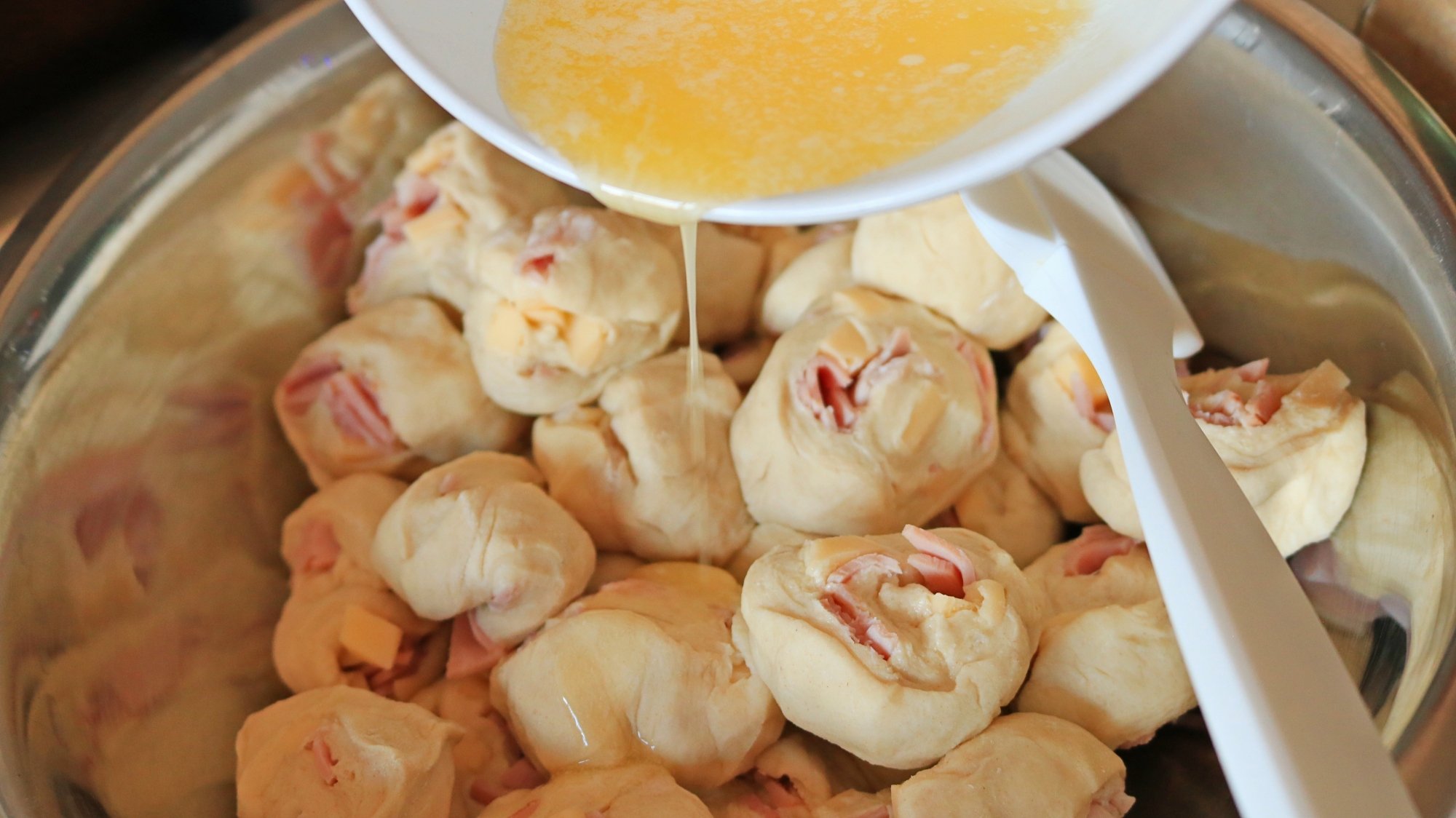 Butter drizzling on dough balls in a mixing bowl.