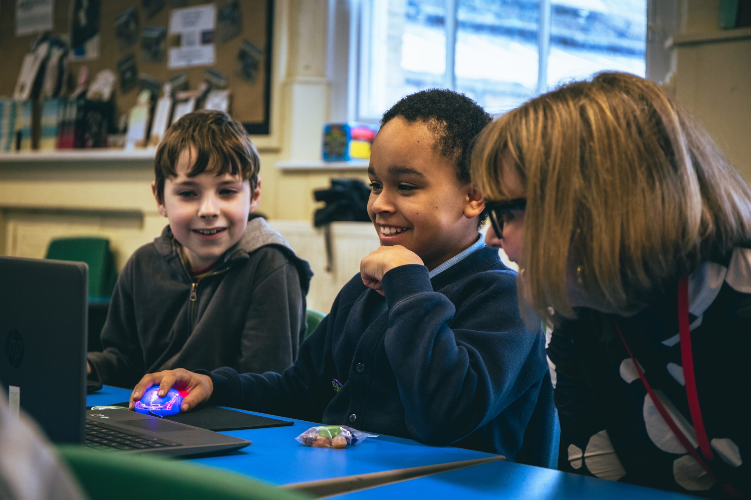 An educator helps two young learners with a coding project in a classroom.