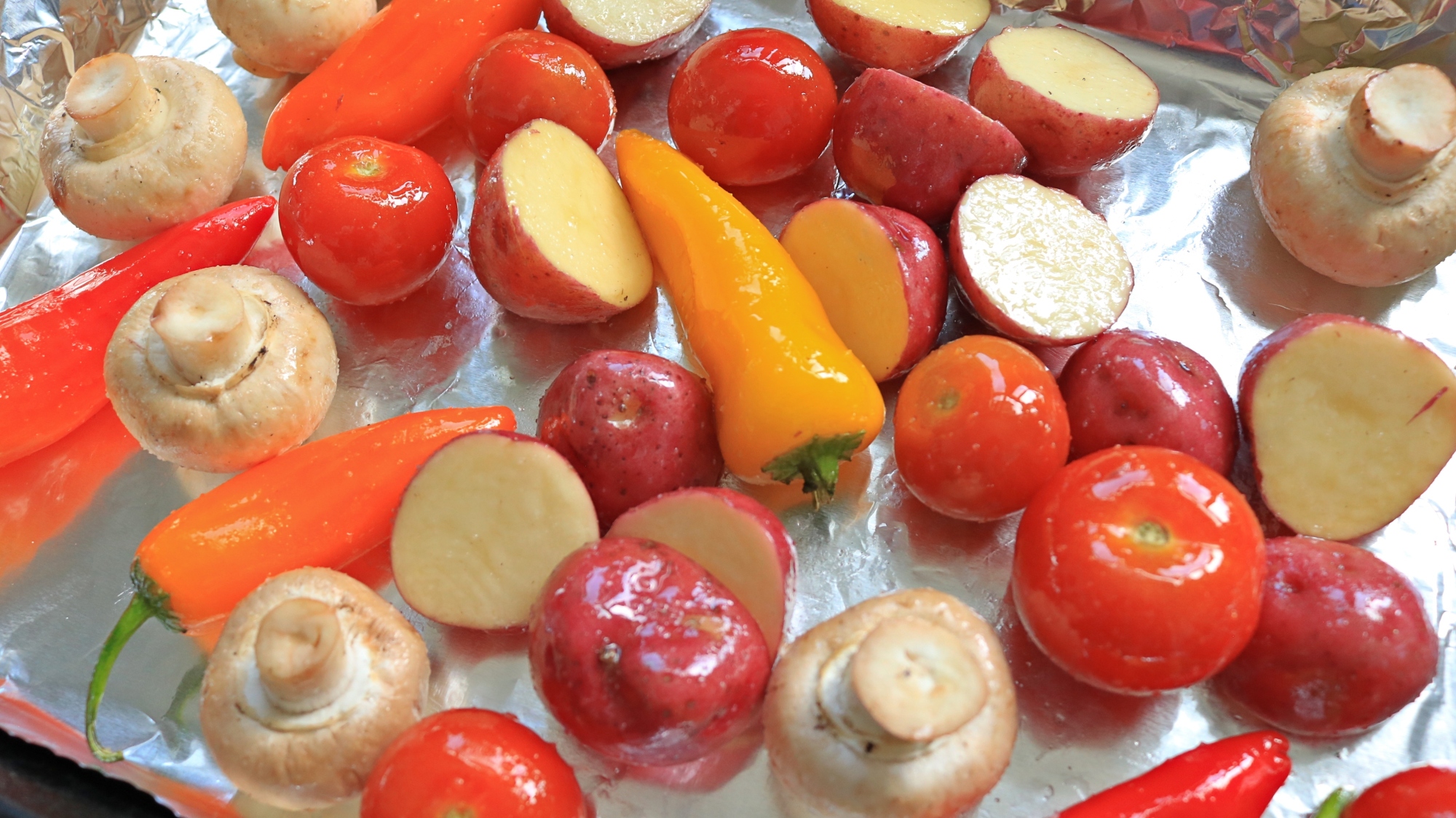 Different vegetables with oil and salt on a foil lined pan.