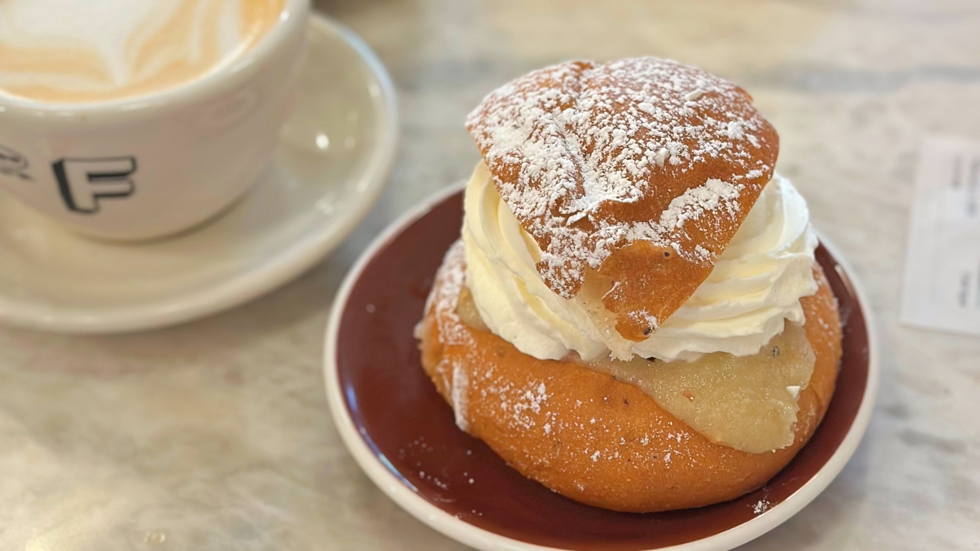 A semlor bun on a plate next to a cup of coffee.