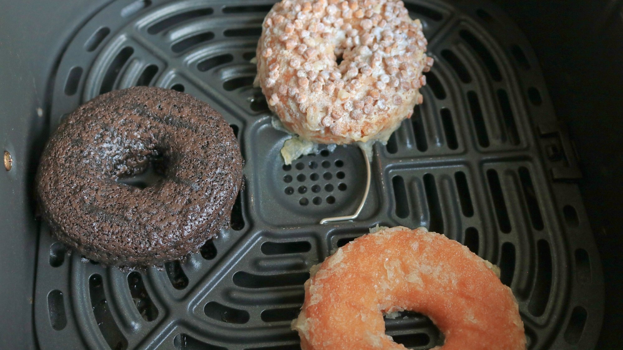 Three doughnuts in an air fryer basket.