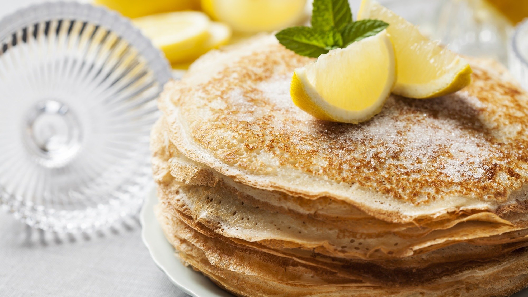 A stack of thin pancakes with lemon wedges on top.