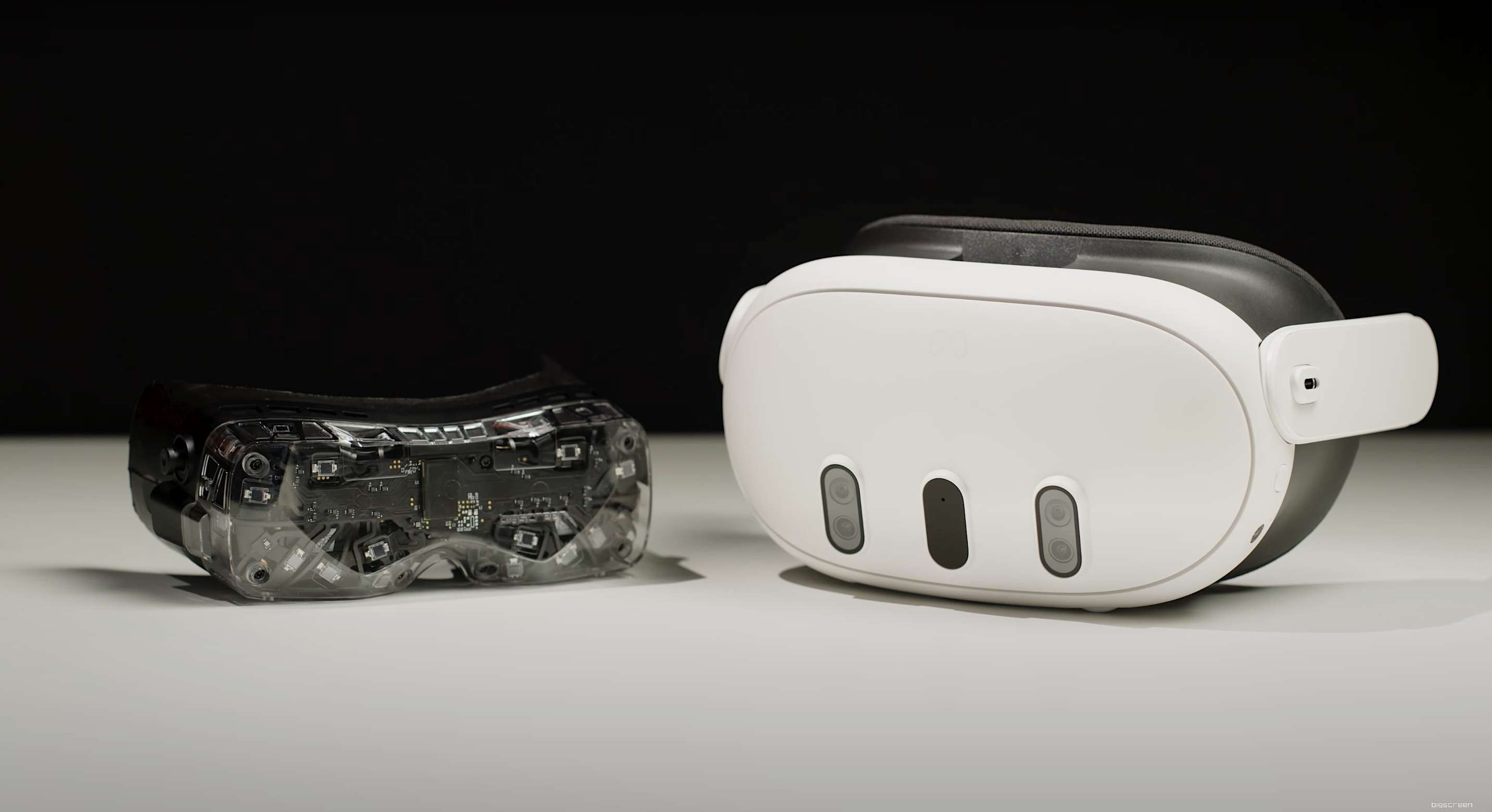 Bigscreen Beyond and Quest 3, lying on a table. The latter VR headset is many times larger.