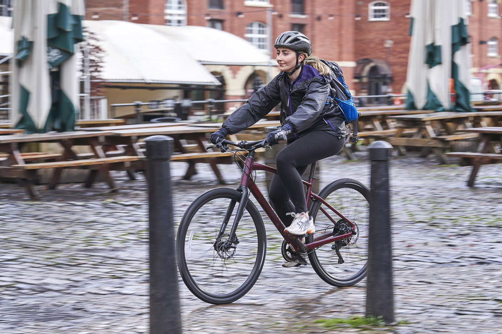 Female cyclist in dark purple jacket riding the Specialized Sirrus X 3.0 commuter bike